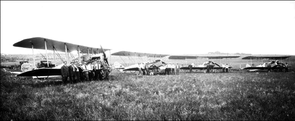 Four Lincoln Standard airplanes parked on a grassy field. Surrounding each plane is a pilot and crew. - Image courtesy of Nebraska History, http://nebraskahistory.pastperfectonline.com